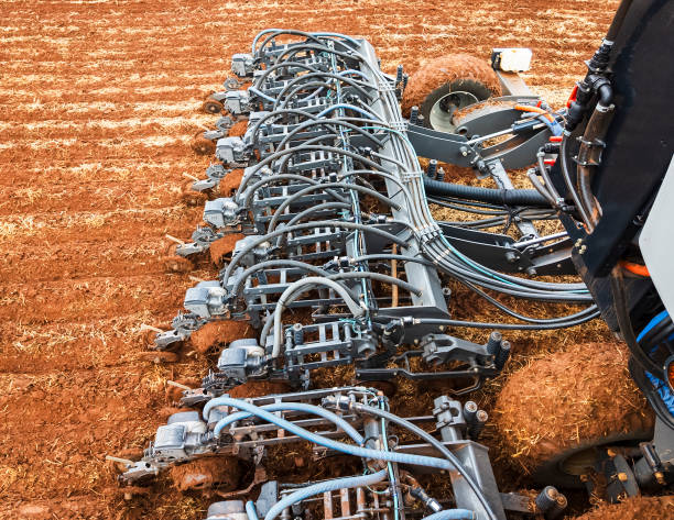 A large, advanced planting machine is seen working on a vast farmland.. The machinery's multiple components and precision technology highlight the efficiency and scale of modern farming practices. The expansive field and clear sky emphasize the rural setting.